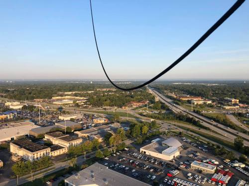 Aerial view of a highway and urban area, with a power line stretching across the foreground under a clear blue sky.