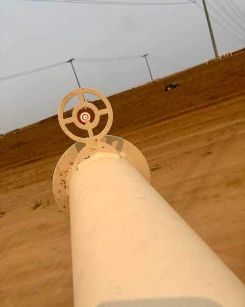 A close-up view of a target sight on a firearm, with a sandy landscape and power lines in the background.