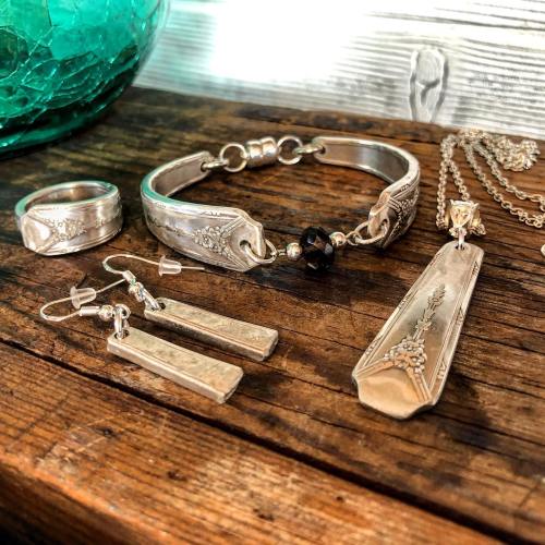 A collection of silver jewelry including a bracelet, ring, earrings, and a pendant on a wooden surface.