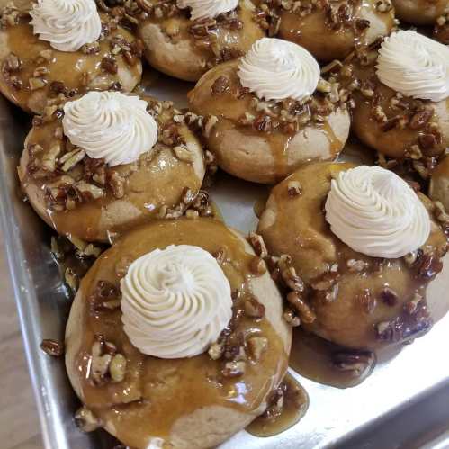 Delicious pastries topped with creamy frosting, caramel sauce, and chopped pecans, arranged on a tray.