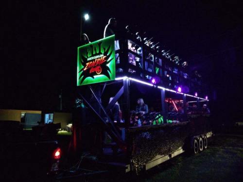 A brightly lit zombie-themed float with people on it, set against a dark night backdrop.