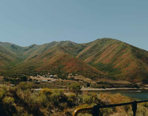 Scenic view of colorful mountains with greenery and a calm lake under a clear blue sky.