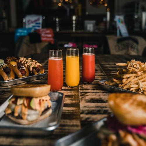 A table with three colorful drinks and a variety of food, including burgers, hot dogs, and fries.