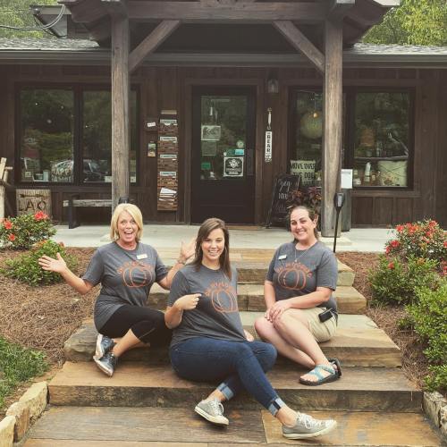 Three women in matching gray t-shirts pose on steps outside a rustic building, smiling and enjoying their time together.