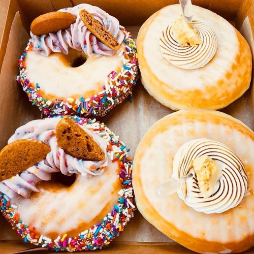 A box of four colorful donuts, two topped with frosting, sprinkles, and cookies, and two with swirls of cream.