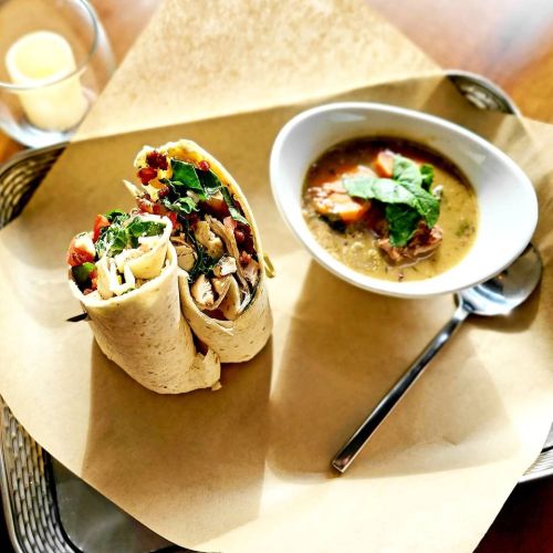 A wrap filled with vegetables and chicken, served with a bowl of soup garnished with herbs on a tray.