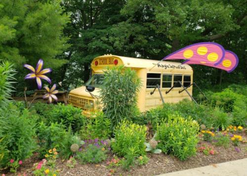 A yellow school bus surrounded by colorful flowers and greenery, with large decorative butterfly wings attached.
