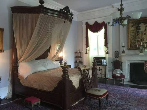 A vintage bedroom featuring a canopy bed, elegant decor, and a fireplace, with rich textiles and antique furniture.