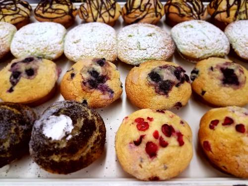 A variety of freshly baked muffins, including blueberry, chocolate, and green tea, displayed on a tray.