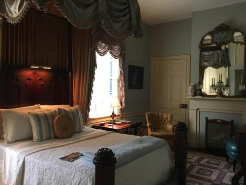 Cozy bedroom with a wooden bed, elegant curtains, a vintage chair, and a decorative fireplace. Soft lighting enhances the ambiance.
