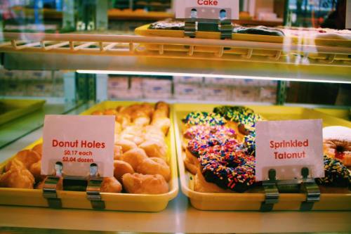 A display case with trays of donut holes and sprinkled tatonut, with price signs in front of each item.