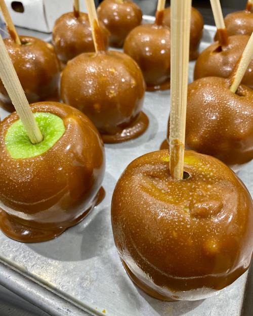 Close-up of caramel-coated apples on a tray, with one apple showing a green interior and wooden sticks for holding.