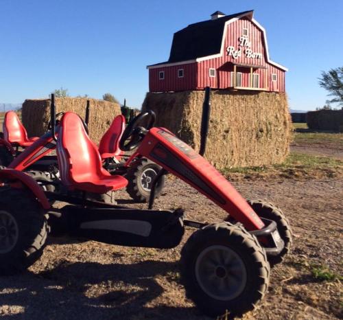 Red go-karts parked near a red barn with hay bales in a sunny outdoor setting.