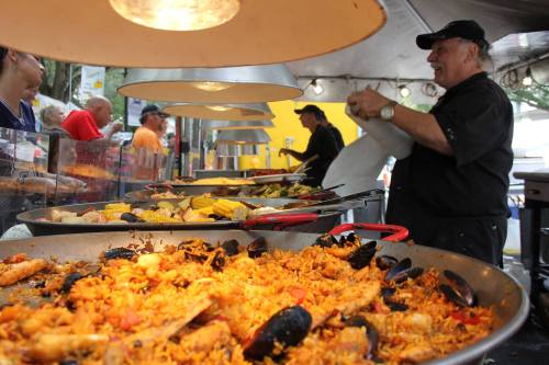 A chef prepares a large paella dish with seafood and vegetables at a bustling outdoor food festival.