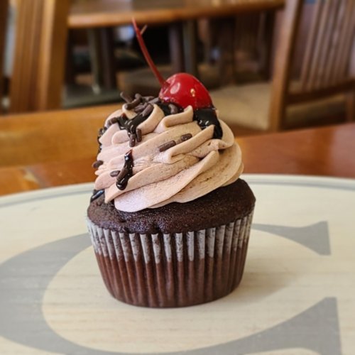 A chocolate cupcake topped with swirls of frosting, chocolate drizzle, and a cherry.