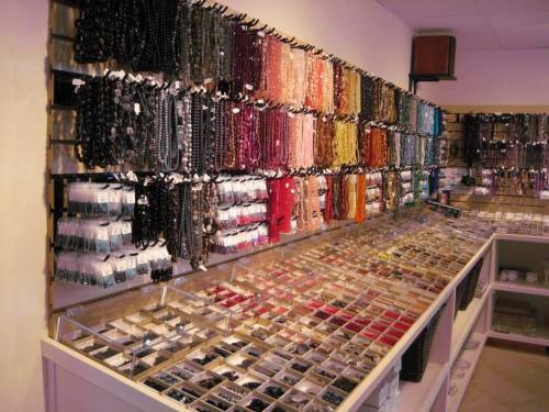 A display of colorful beads and jewelry supplies arranged on shelves and in clear containers in a craft store.