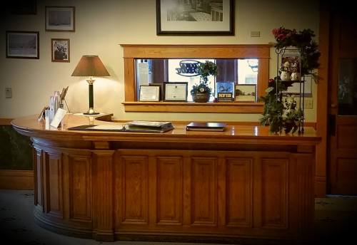 Wooden reception desk with a lamp, framed photos, and decorative plants in a warmly lit office setting.