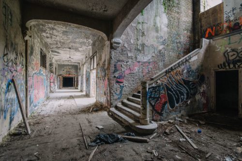 Abandoned interior with graffiti-covered walls, a staircase, and debris scattered on the floor.