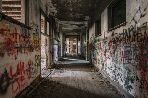 A dimly lit, abandoned hallway with graffiti-covered walls and debris on the floor.