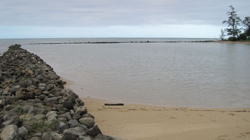 A serene beach scene with a rocky shoreline and calm waters under a hazy sky.