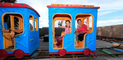A girl and a woman smile and wave from a colorful blue train ride at an amusement park.