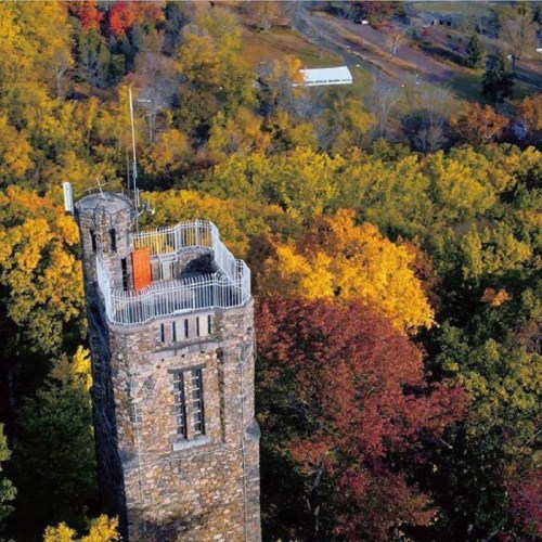 Aerial view of a stone tower surrounded by vibrant autumn foliage in a wooded area.