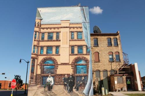 A large mural depicting a historic building on the side of a brick structure, with a clear blue sky above.