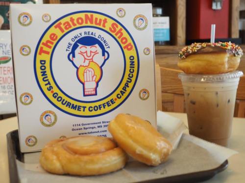A box of donuts from TatoNut Shop with two donuts on a plate and an iced coffee in a cup, set in a cozy café.