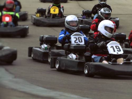 A group of go-karts racing on a track, with drivers wearing helmets and colorful racing suits.