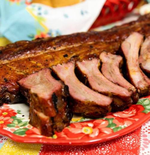 A platter of sliced, smoked ribs with a glossy glaze, served on a floral-patterned plate.