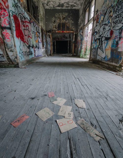 An abandoned room with graffiti-covered walls and scattered, worn playing cards on the wooden floor.
