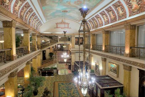 Elegant hotel lobby with ornate architecture, chandeliers, and decorative ceilings, featuring lush greenery and intricate details.