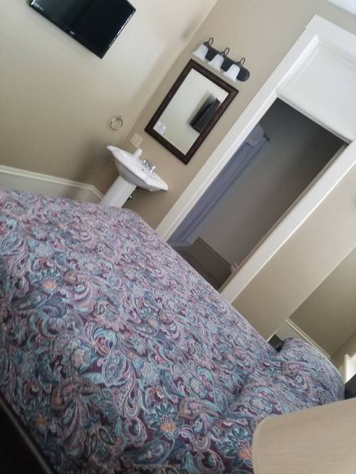 A cozy bedroom with a patterned bedspread, a small sink, a mirror, and a doorway leading to a bathroom.