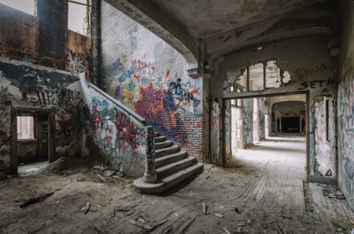 Abandoned building interior with graffiti-covered walls, a staircase, and debris scattered on the floor.