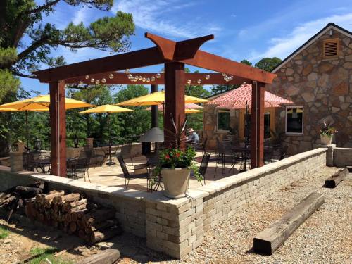 Outdoor patio with a wooden pergola, yellow umbrellas, stone walls, and seating, surrounded by trees and blue sky.