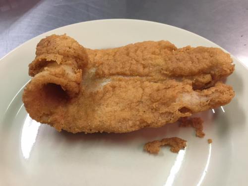 A piece of fried fish on a plate, with a crispy golden-brown coating and a unique shape.