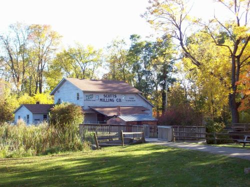 A rustic building with "Scott's Milling Co." sign, surrounded by trees in autumn colors and a grassy area.