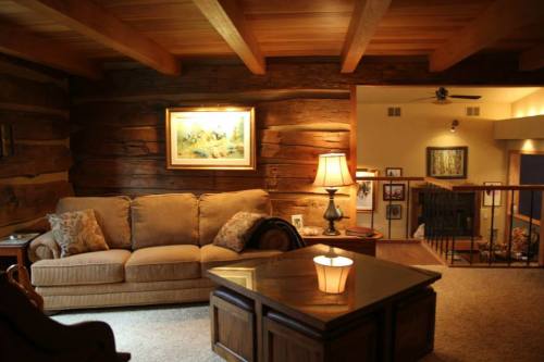 Cozy living room with wooden beams, a sofa, a coffee table, and warm lighting, featuring rustic decor and artwork.
