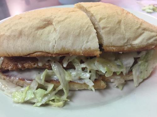 A close-up of a sandwich with crispy filling, lettuce, and creamy sauce, served in a soft, split bread roll.