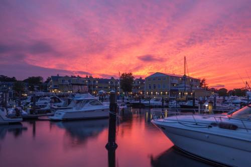 A vibrant sunset over a marina, reflecting colorful skies on calm waters with boats docked along the shore.