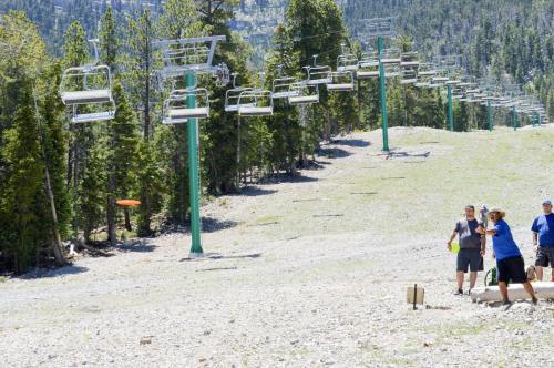 A group of people playing disc golf on a grassy slope with ski lift chairs in the background.