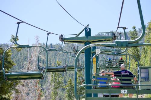A ski lift with empty chairs ascending a mountain, surrounded by trees and a clear blue sky.