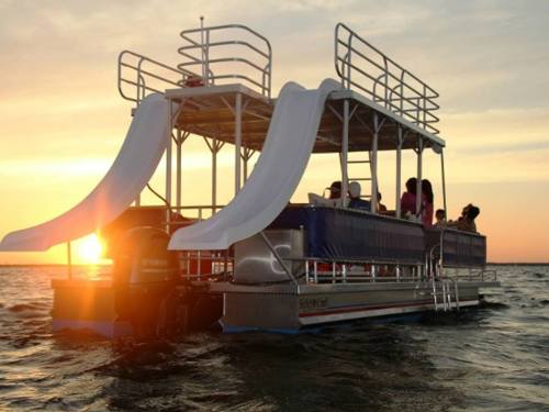 A party boat with water slides at sunset, surrounded by calm waters and people enjoying the ride.