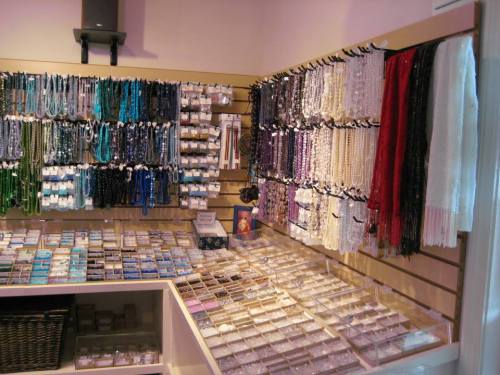 A display of colorful beads and jewelry supplies on shelves and in containers, showcasing various materials and textures.