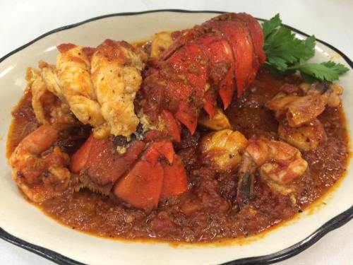A plate of lobster and shrimp in a rich tomato sauce, garnished with fresh herbs.