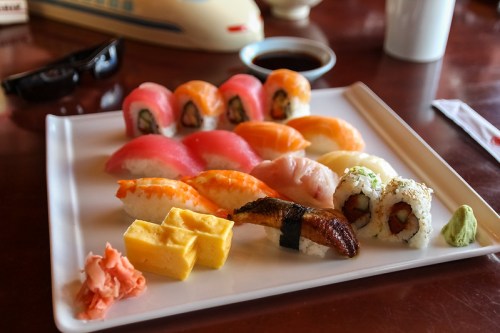 A plate of assorted sushi, including rolls, sashimi, and tamago, with wasabi and pickled ginger on the side.