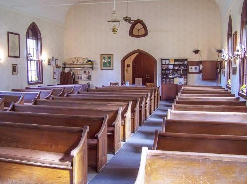 Interior of a church featuring wooden pews, a simple altar, and decorative wall art. Natural light filters in through windows.
