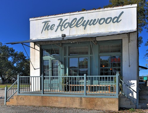 A vintage storefront with the sign "The Hollywood" and large windows, set against a clear blue sky.