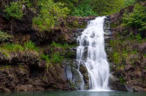 A serene waterfall cascading over rocky cliffs into a tranquil pool, surrounded by lush greenery.