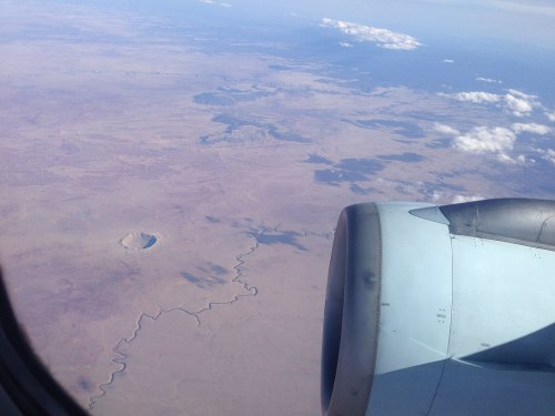 Aerial view of a vast desert landscape with a river winding through and an airplane wing in the foreground.